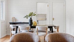 A dining area with a table, chairs, a vase with plants, and a kitchen in the background. - South Hobart Designer Retreat (South Hobart)