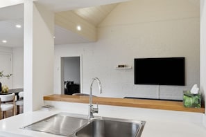 Eine moderne Küche mit Spüle aus Edelstahl, Arbeitsplatte aus Holz und einem flachbildschirmfernseher an der Wand.