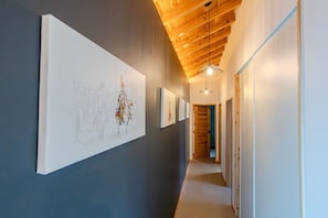 A hallway with artwork on the walls, wooden ceiling beams, and a hanging light fixture. - Guestready - Casa do Lanceiro by Cavalhadas House (Ribeira Grande)