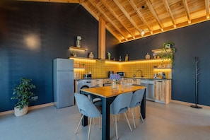 A modern kitchen with a wooden ceiling, a dining area with a table and chairs, and a washing machine. - GuestReady - Casa do Cavaleiro by Cavalhadas House (Ribeira Grande)