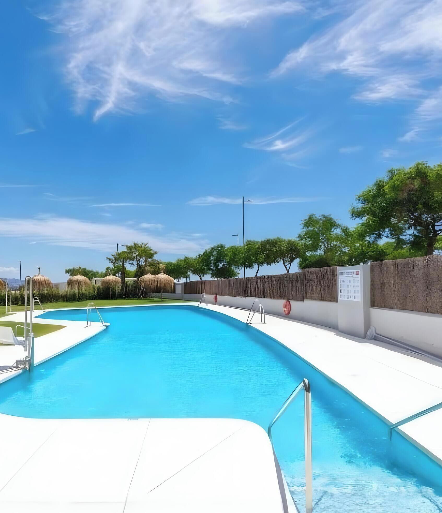 Una piscina con cielo azul despejado, rodeada de árboles y una valla de madera.