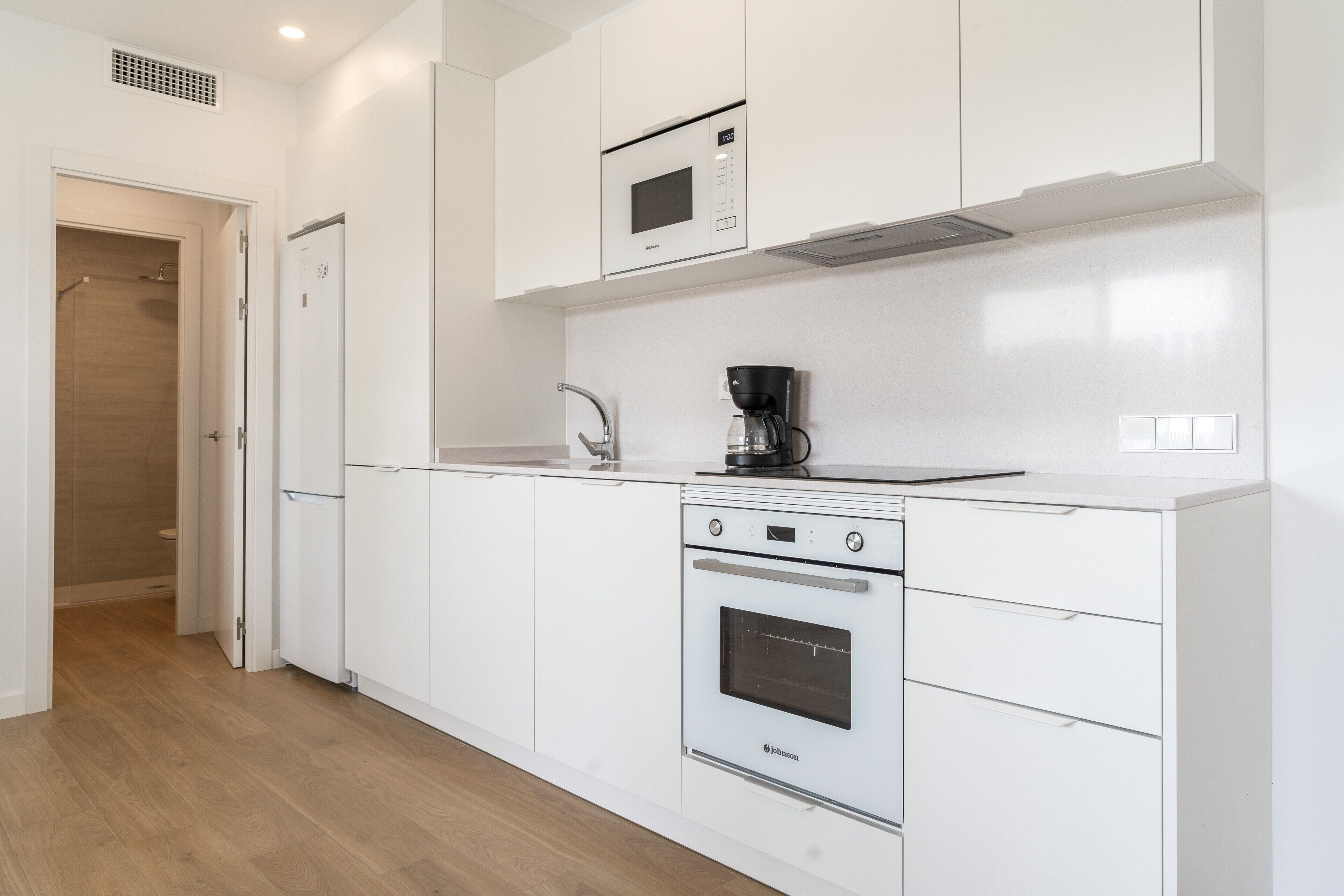 Een moderne keuken met witte kastjes, een inbouwoven, een magnetron en een koffiezetapparaat.