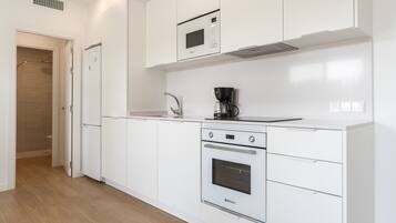 Een moderne keuken met witte kastjes, een inbouwoven, een magnetron en een koffiezetapparaat.