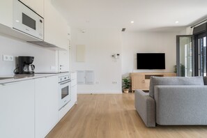 A modern kitchen with a coffee machine, a stove, and a built-in oven. There is a dining area with a sofa and a television.