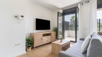 A modern living room with a flat-screen TV, a wooden cabinet, a grey sofa, and a sliding glass door leading to an outdoor balcony.