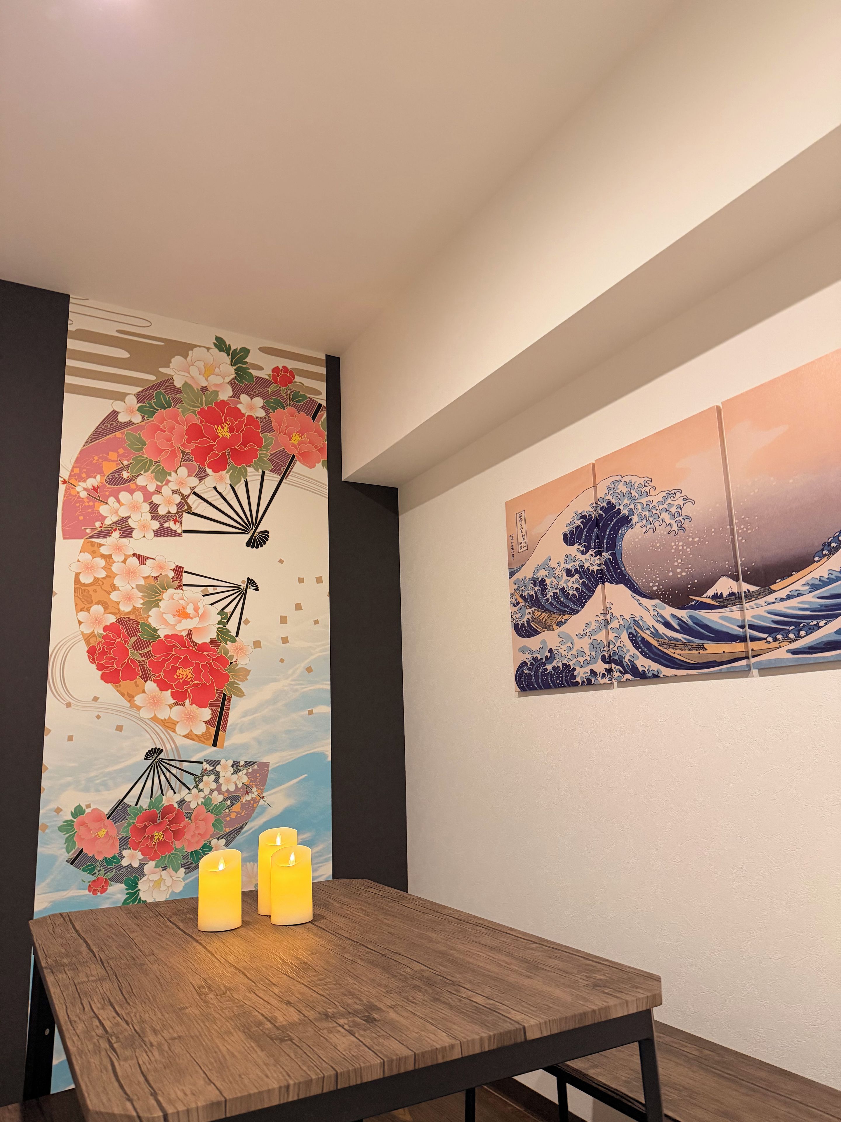Un comedor con una mesa de madera, dos velas y dos obras de arte en la pared que representan escenas tradicionales japonesas.