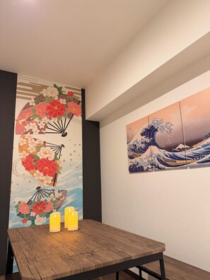 Un comedor con una mesa de madera, dos velas y dos obras de arte en la pared que representan escenas tradicionales japonesas.