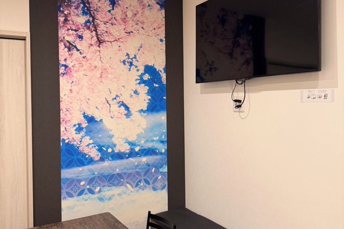Una habitación con una mesa de comedor de madera, tres velas, un televisor montado en la pared y un cuadro abstracto grande.