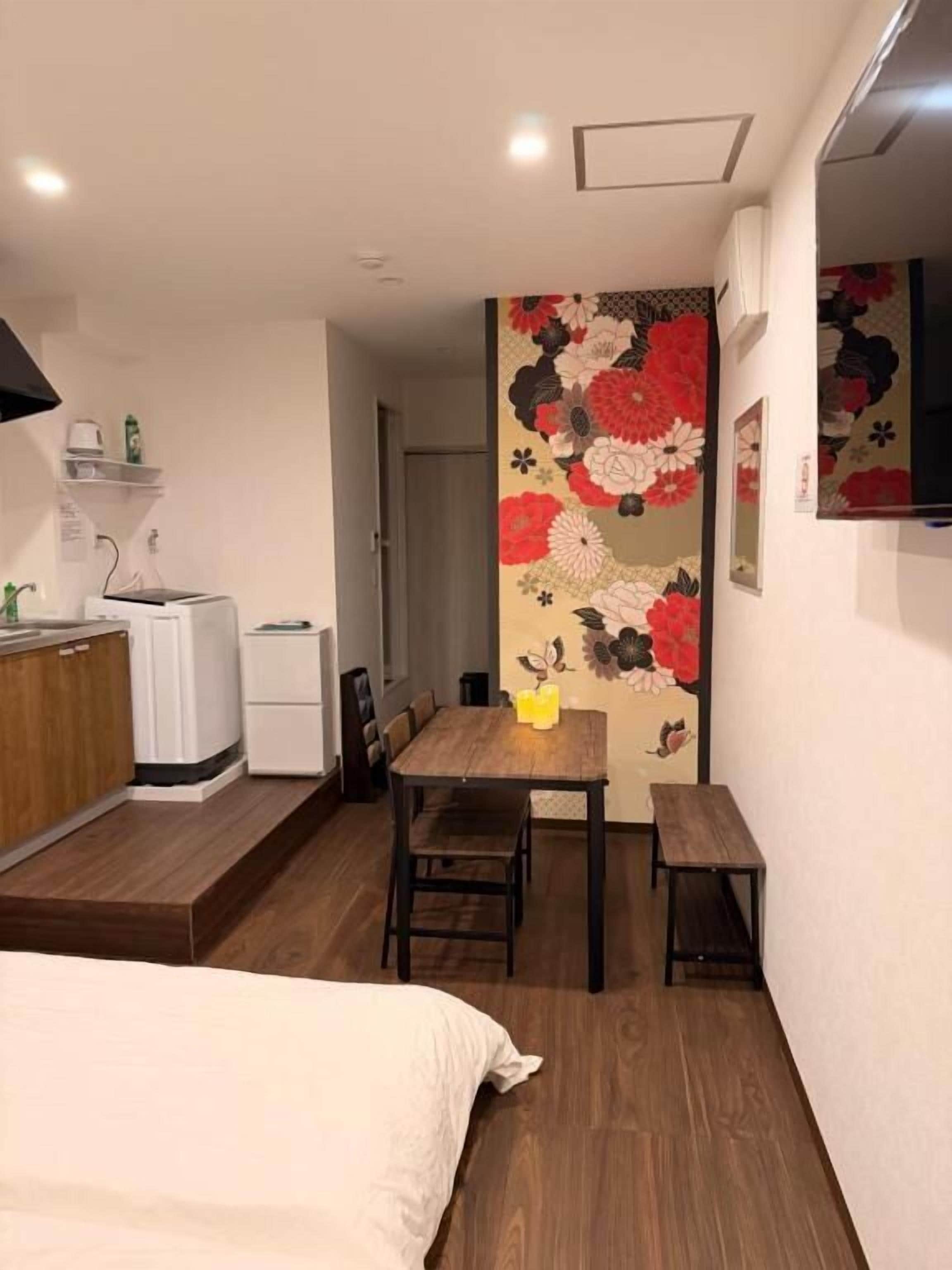 Habitación de hotel pequeña con cama, una mesita, un banco, microondas y refrigerador.