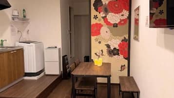 Habitación de hotel pequeña con cama, una mesita, un banco, microondas y refrigerador.