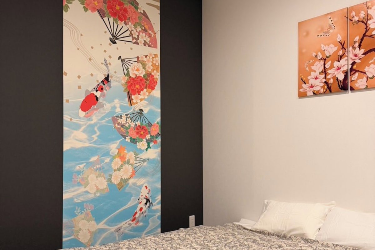 Un dormitorio con una cama, un mural grande en la pared y un cuadro más pequeño.