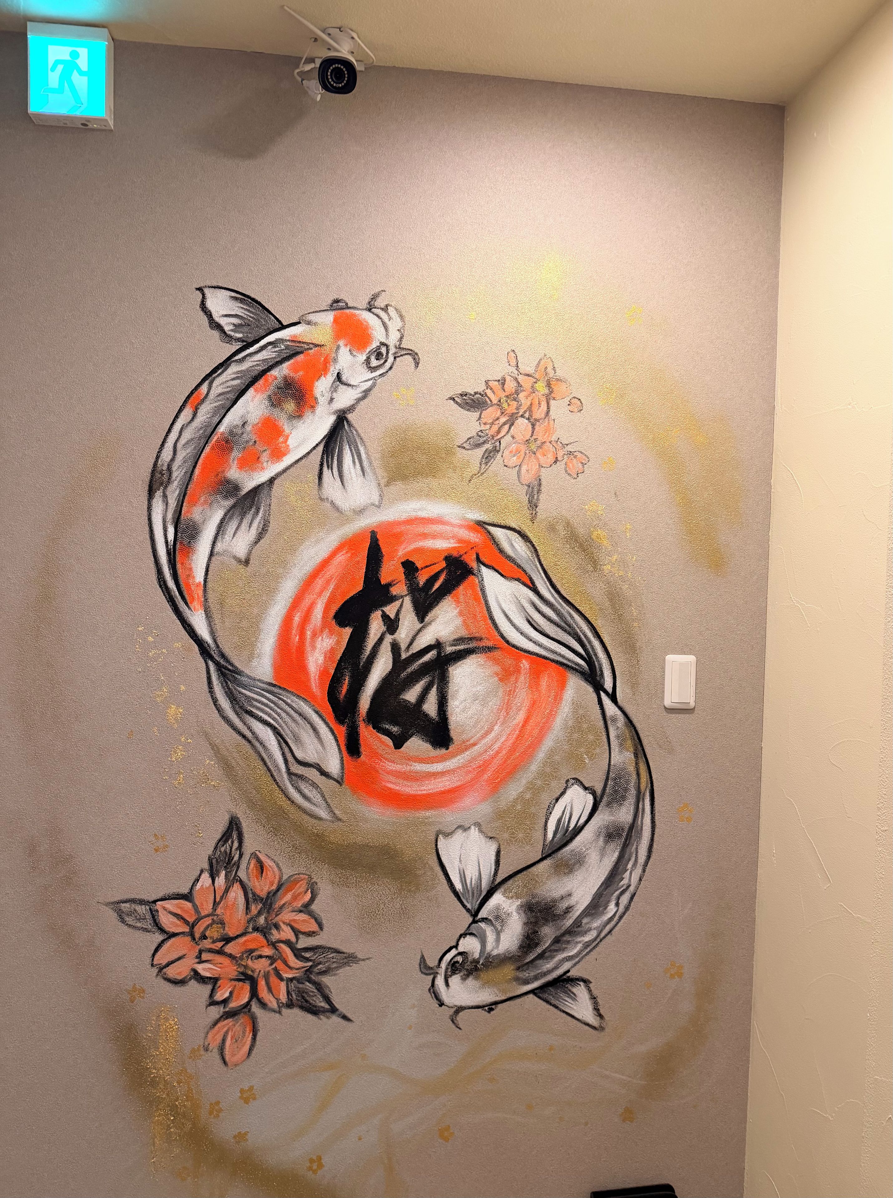Un muro con un murale di carpe koi, una presa elettrica e un rilevatore di fumo.