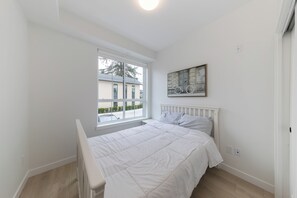 Une chambre avec une grande fenêtre, un lit recouvert de linge de lit blanc et une œuvre d’art accrochée au mur.