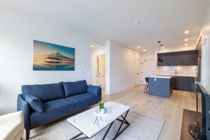 A modern living room with a sofa, a coffee table, and a painting of a mountain. - Brand New Luxury 2 Bedroom Surrey/White Rock (Surrey)