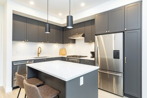 A modern kitchen with grey cabinets, stainless steel appliances, and a central island with two chairs. - Brand New Luxury 2 Bedroom Surrey/White Rock (Surrey)