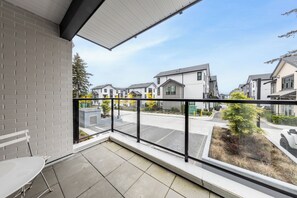 Un balcon donnant sur une rue résidentielle, un sol carrelé et une rambarde en métal.