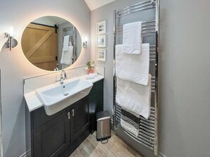 Ein modernes Badezimmer mit einem runden Spiegel, einem Waschbecken, dunklen Schränken, einem Handtuchhalter und einem Papierkorb.