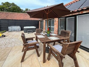 Eine Terrasse im Freien mit einem Holztisch und -stühlen, einem Whirlpool und einem überdachten Bereich mit einem großen Sonnenschirm.