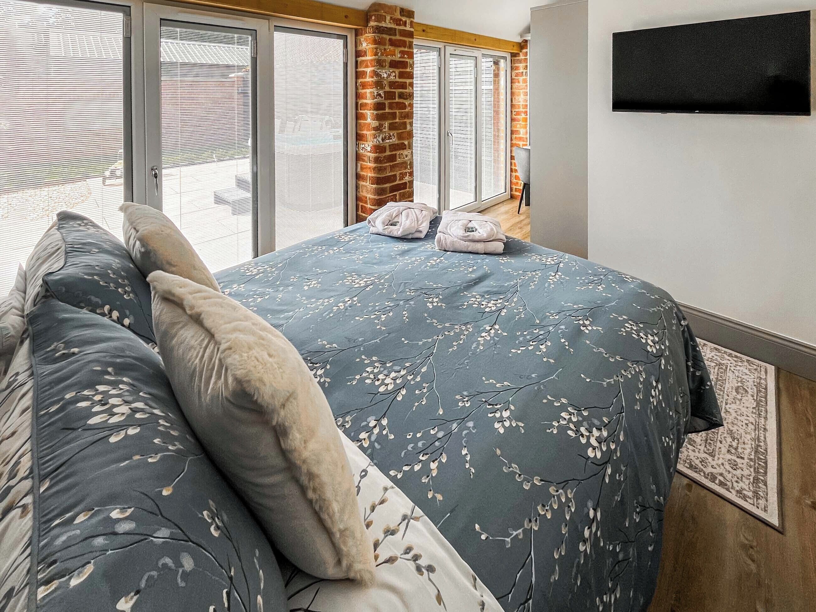 A bedroom with a large bed, a flat-screen TV mounted on the wall, and a view through the window.