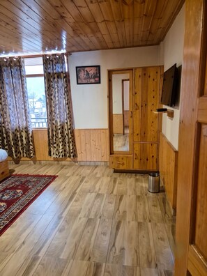 A room with wooden flooring, a red patterned rug, a wardrobe with a mirror, and a television mounted on the wall. - OnlyStay Persimmon Farmstead (Manali)
