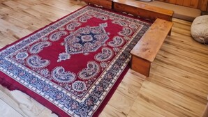 A room with a wooden floor, a red patterned rug, a bench, and a window with curtains. - OnlyStay Persimmon Farmstead (Manali)