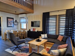 A modern living room with a sofa, armchair, dining table, and TV. - Kivakka C 6 | 2BR Cabin near Lake | 2 Ski Passes (Kuusamo)