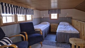 Ett litet rum med två sängar, en stol, ett litet bord och ett fönster.