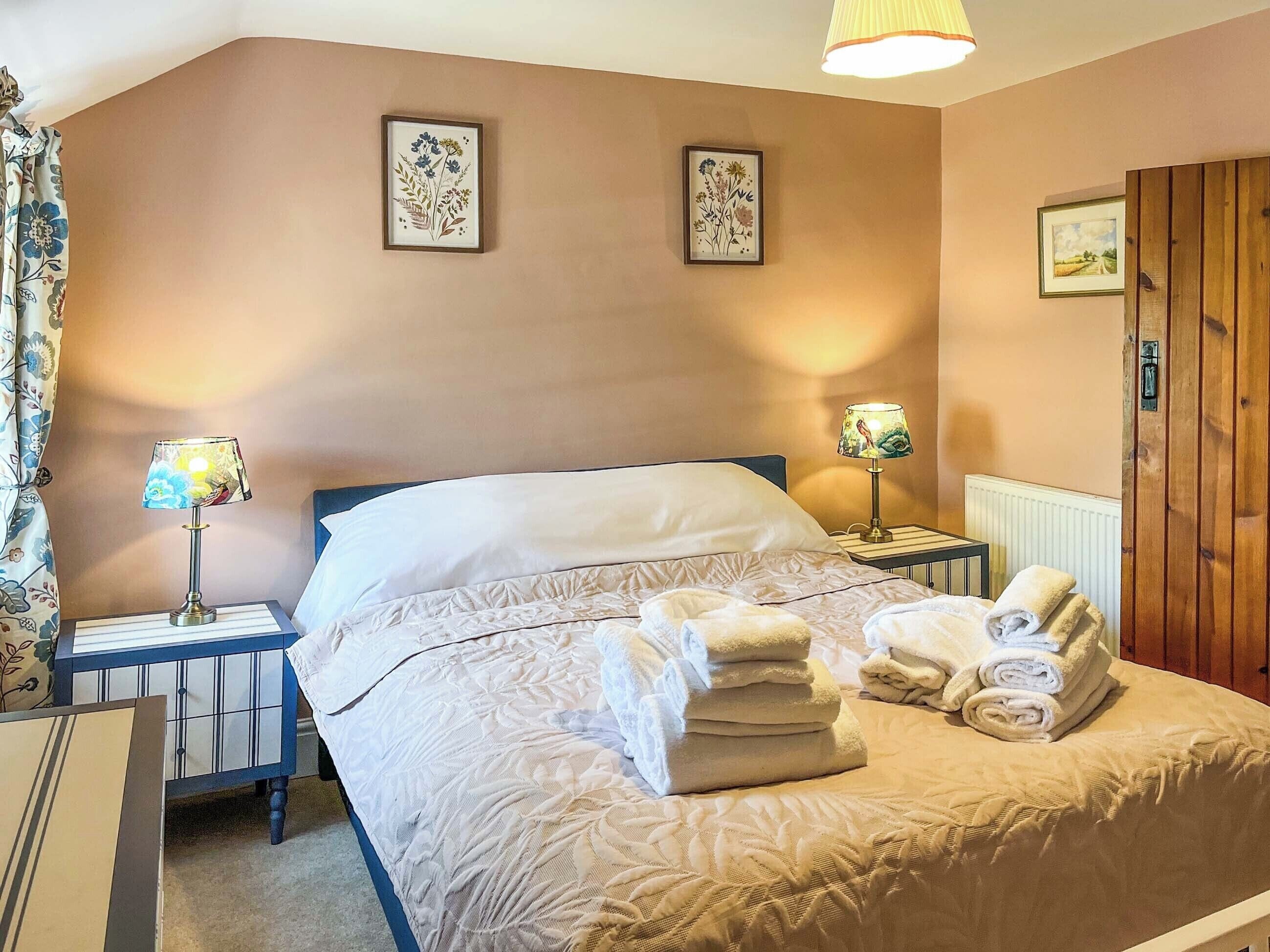 Habitación de hotel con cama, dos lámparas de noche, un juego de toallas y un cuadro de flores en la pared.