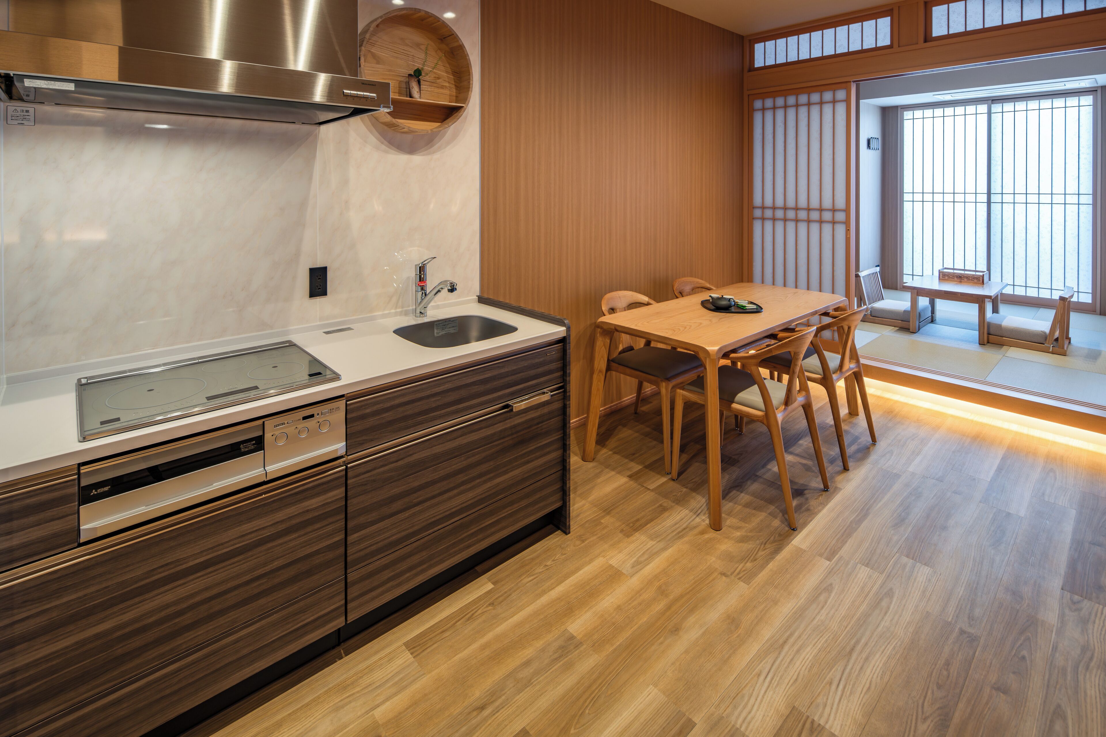 A modern kitchen with a built-in oven, a stainless steel range hood, and a wooden dining table with chairs.