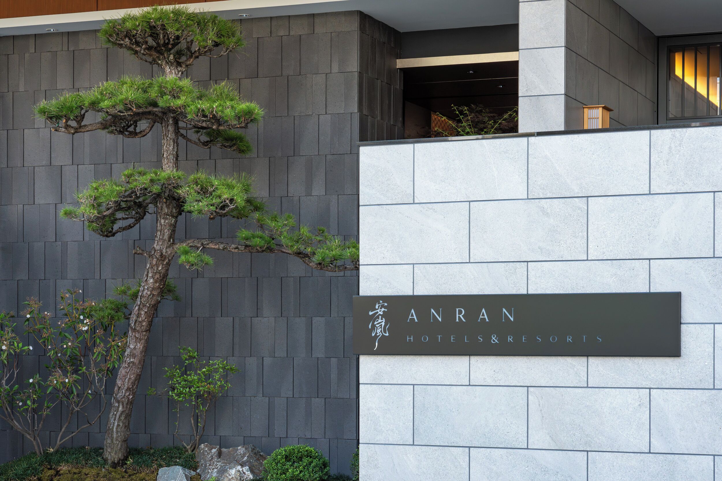 A modern building facade with a large bonsai tree and a sign for 'ANRAN HOTELS & RESORTS'.