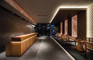 A modern reception area with a wooden reception desk, seating area with wicker chairs, and patterned walls. - Anran Hotels&Resorts (OSAKA)