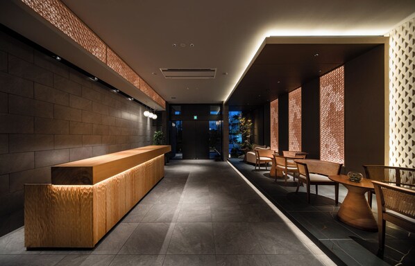 A modern reception area with a wooden reception desk, seating area with wicker chairs, and patterned walls. - Anran Hotels&Resorts (OSAKA)
