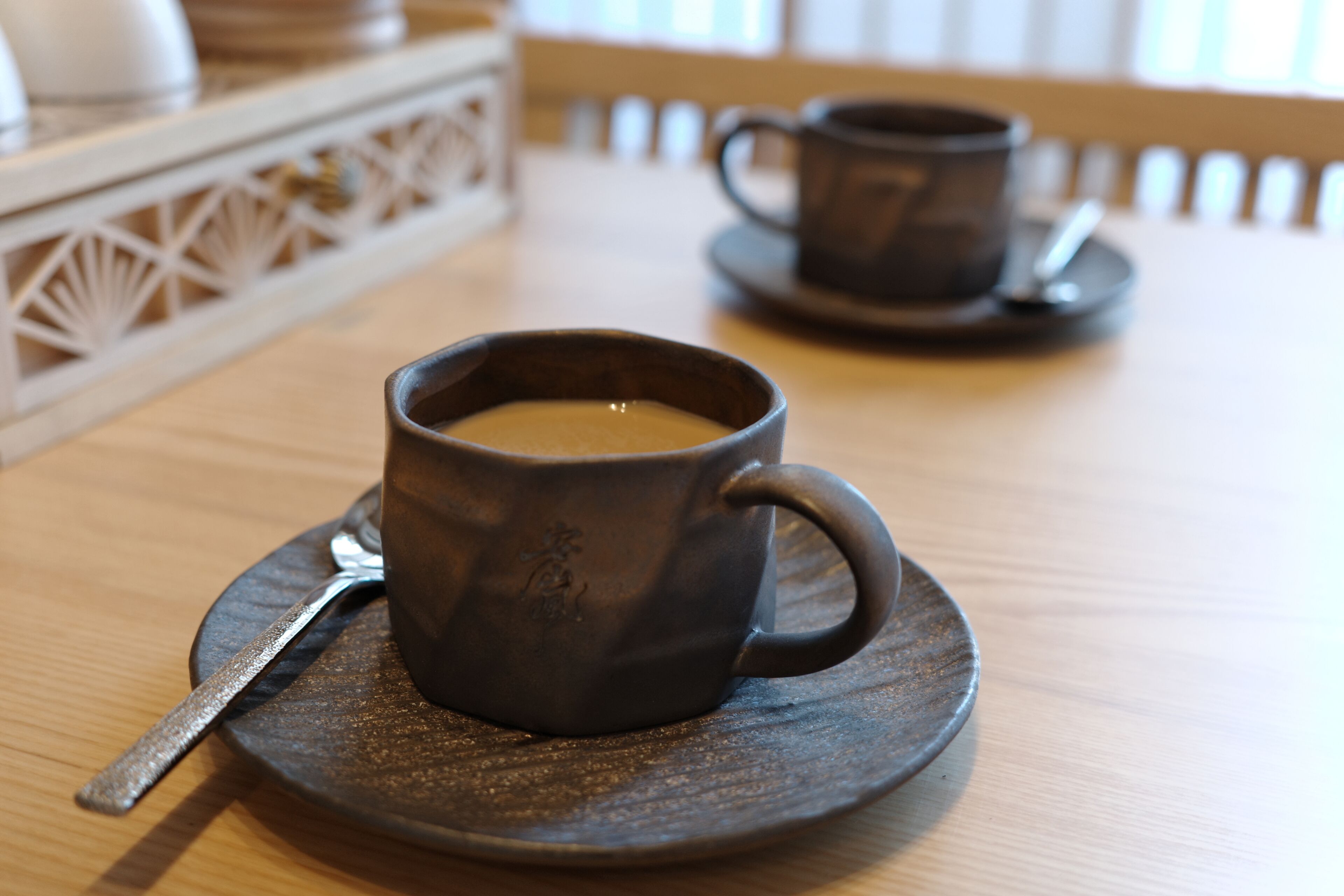 Eine dunkle Keramiktasse mit Löffel auf einem Untertasse, platziert auf einem Holztisch.