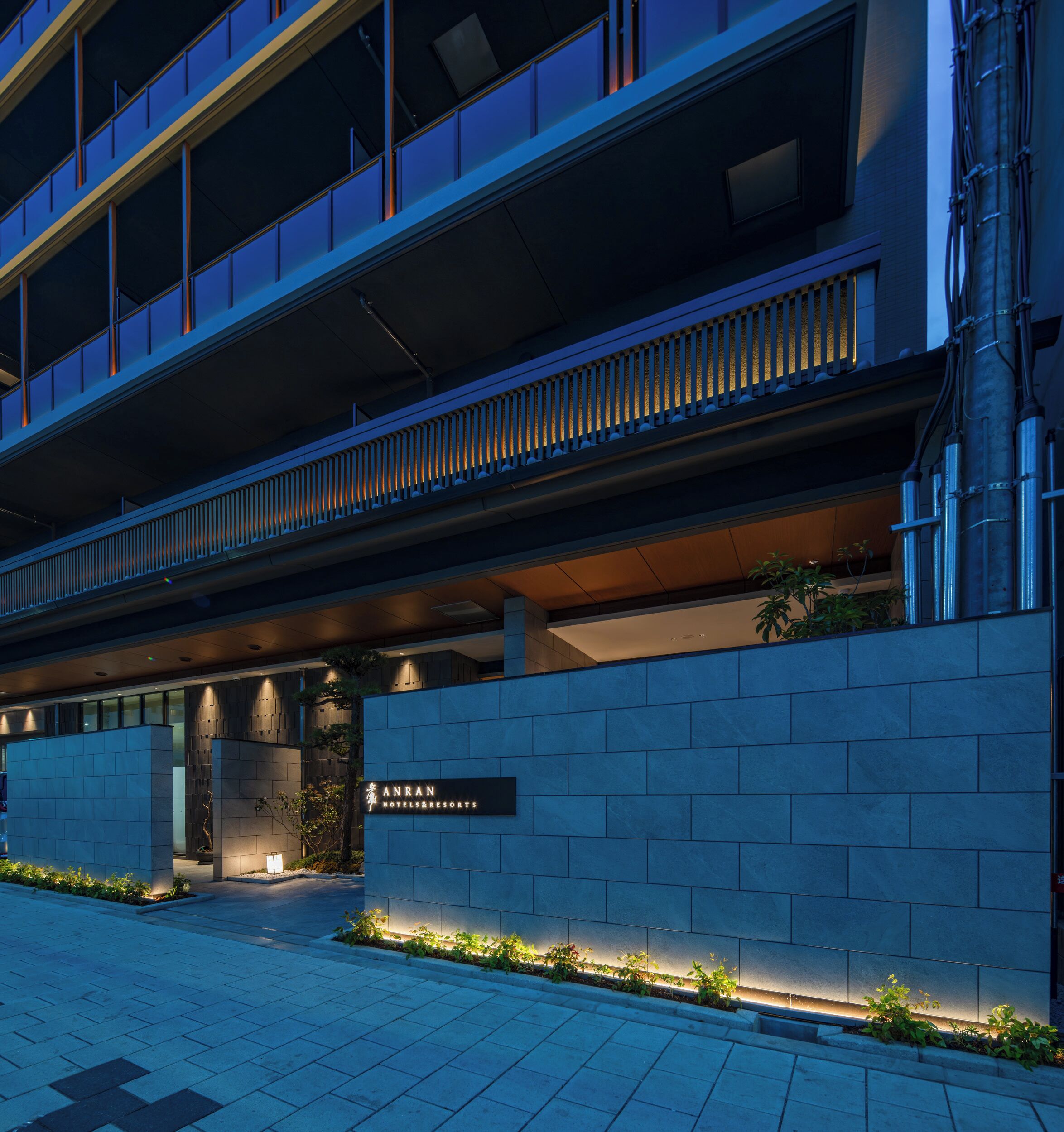 A modern hotel entrance with a sign for 'Anran Hotels & Resorts,' a covered walkway, and a landscaped area with plants.