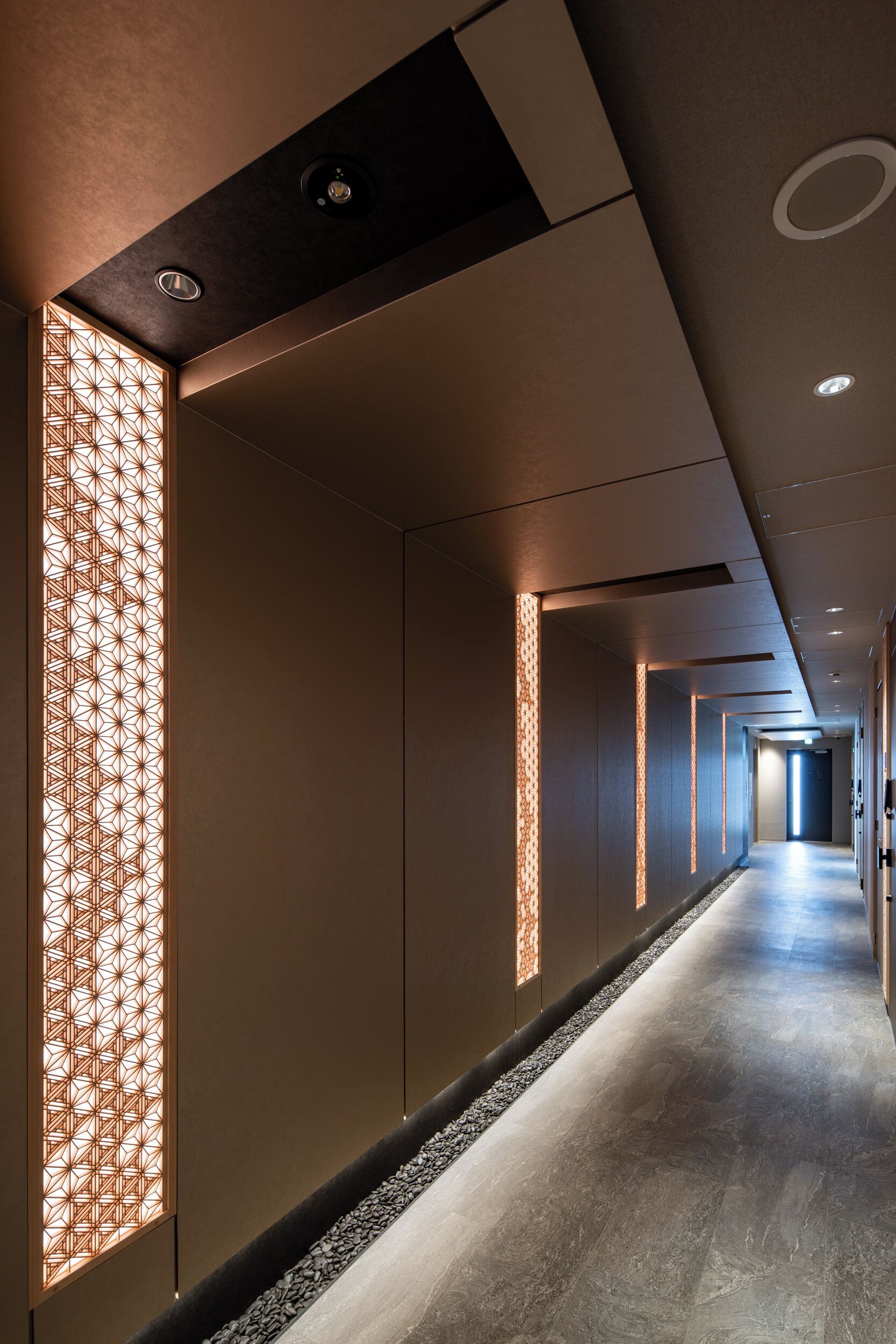 A modern hotel corridor with a long, straight hallway, recessed lighting, and decorative wall panels.