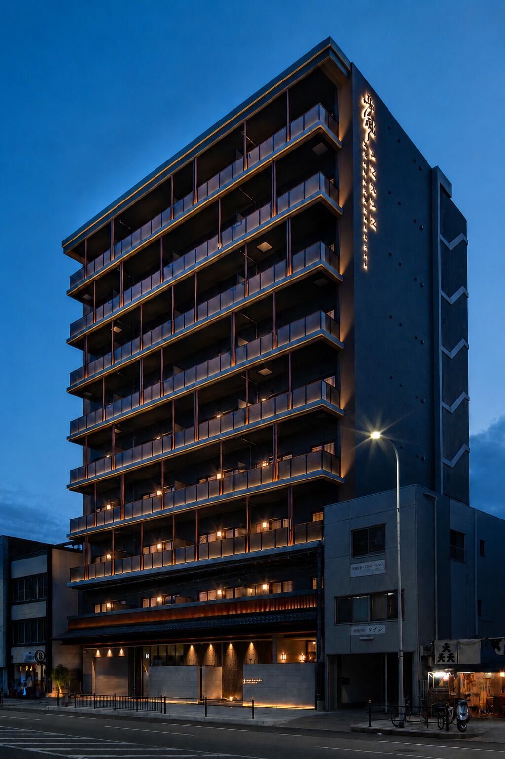 A multi-story hotel with balconies, a ground-level entrance, and a sign with Japanese characters.