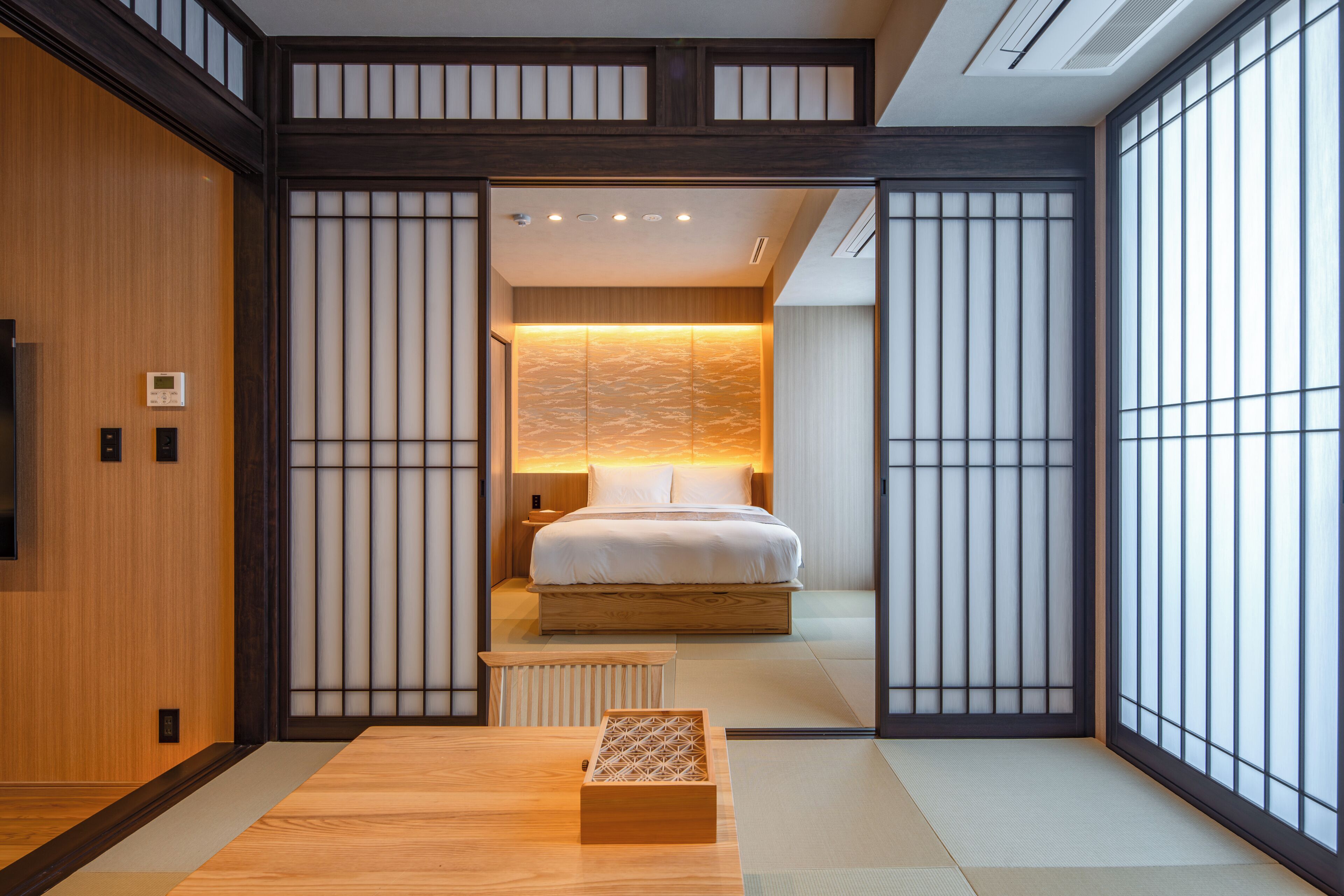 Um quarto tradicional japonês com piso de tatame, uma cama com roupa de cama branca e uma porta de papel deslizante estilo shoji.