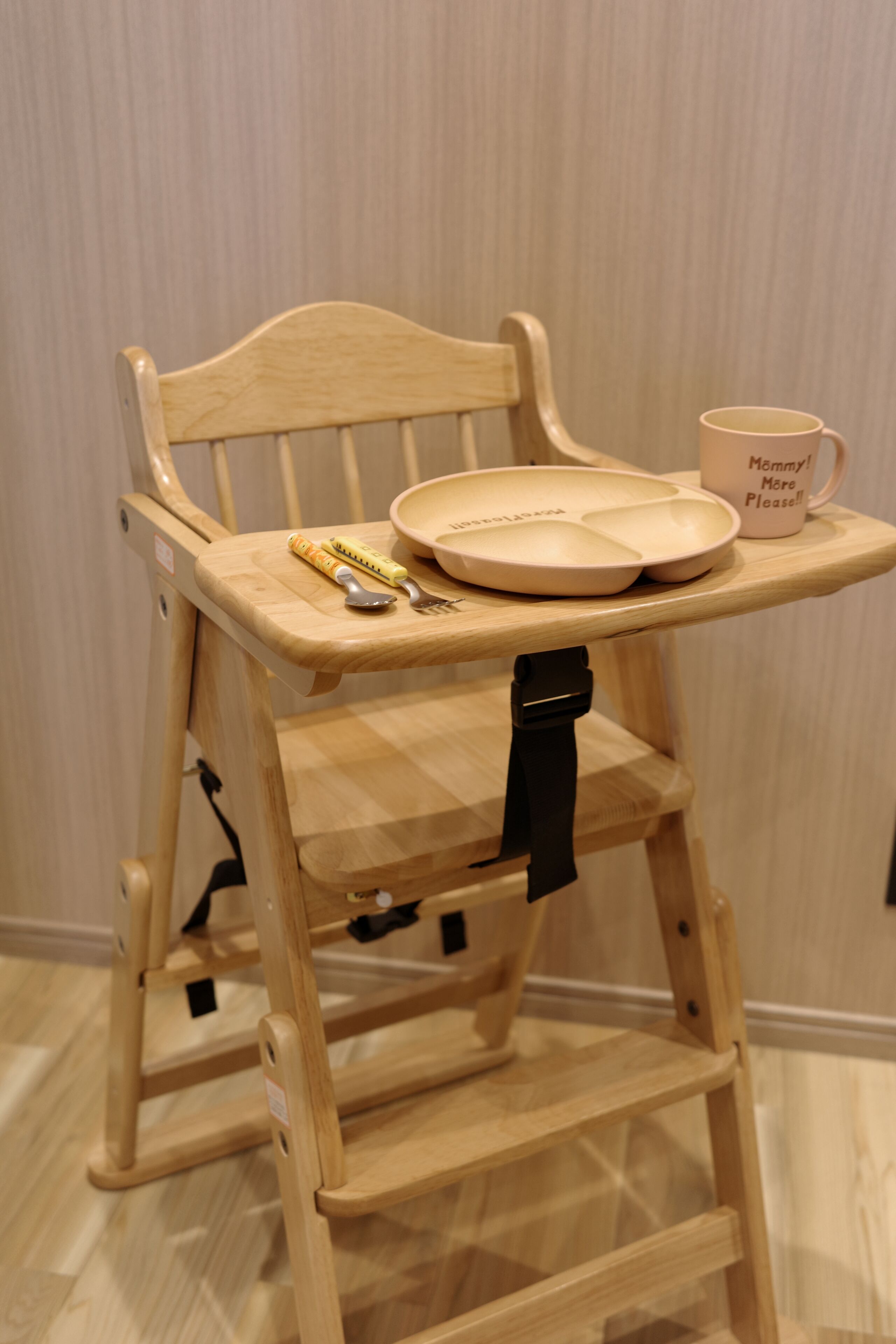 Una trona de madera con una mesita, una cuchara, un tenedor y una taza con texto.