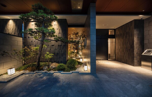 A modern building with a stone facade, a large tree, and a well-lit entrance area.