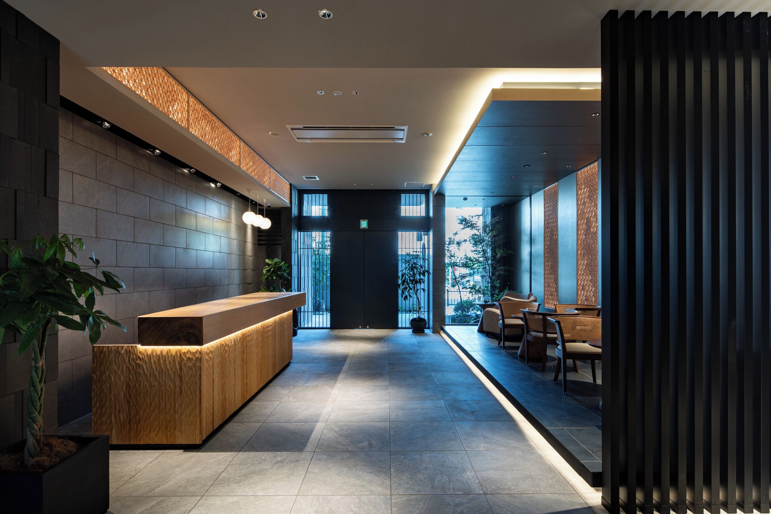 A modern hotel lobby with a reception desk, seating area, and large windows.
