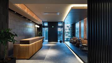 A modern hotel lobby with a reception desk, seating area, and large windows.