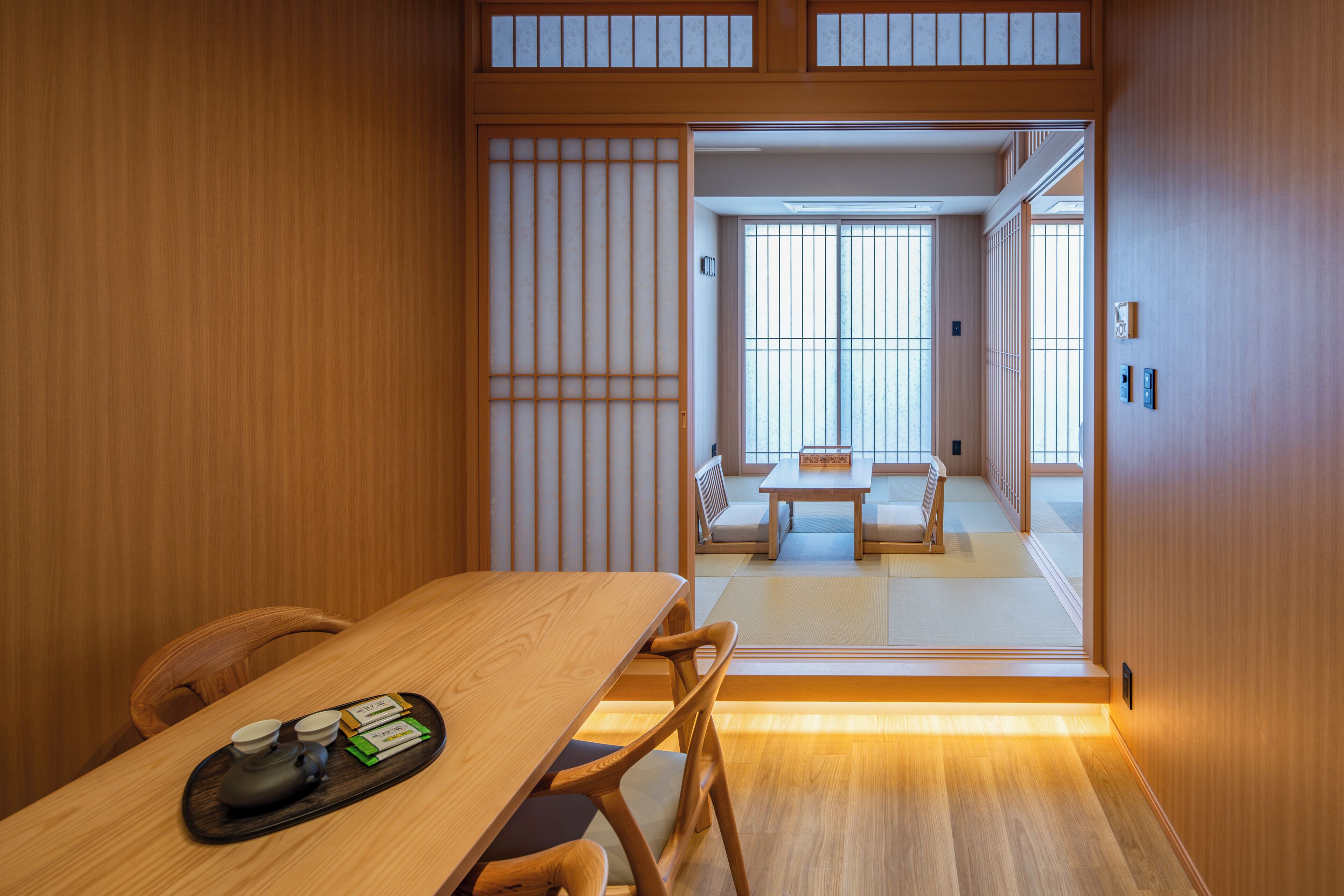 Et traditionelt japansk rum med tatamigulv, et lavt bord med et te-service og skydedøre, der fører til et spiseområde.