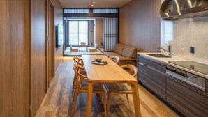 Una cocina moderna con armarios de madera, un comedor con mesa y sillas de madera, y vista hacia un salón con puertas correderas.