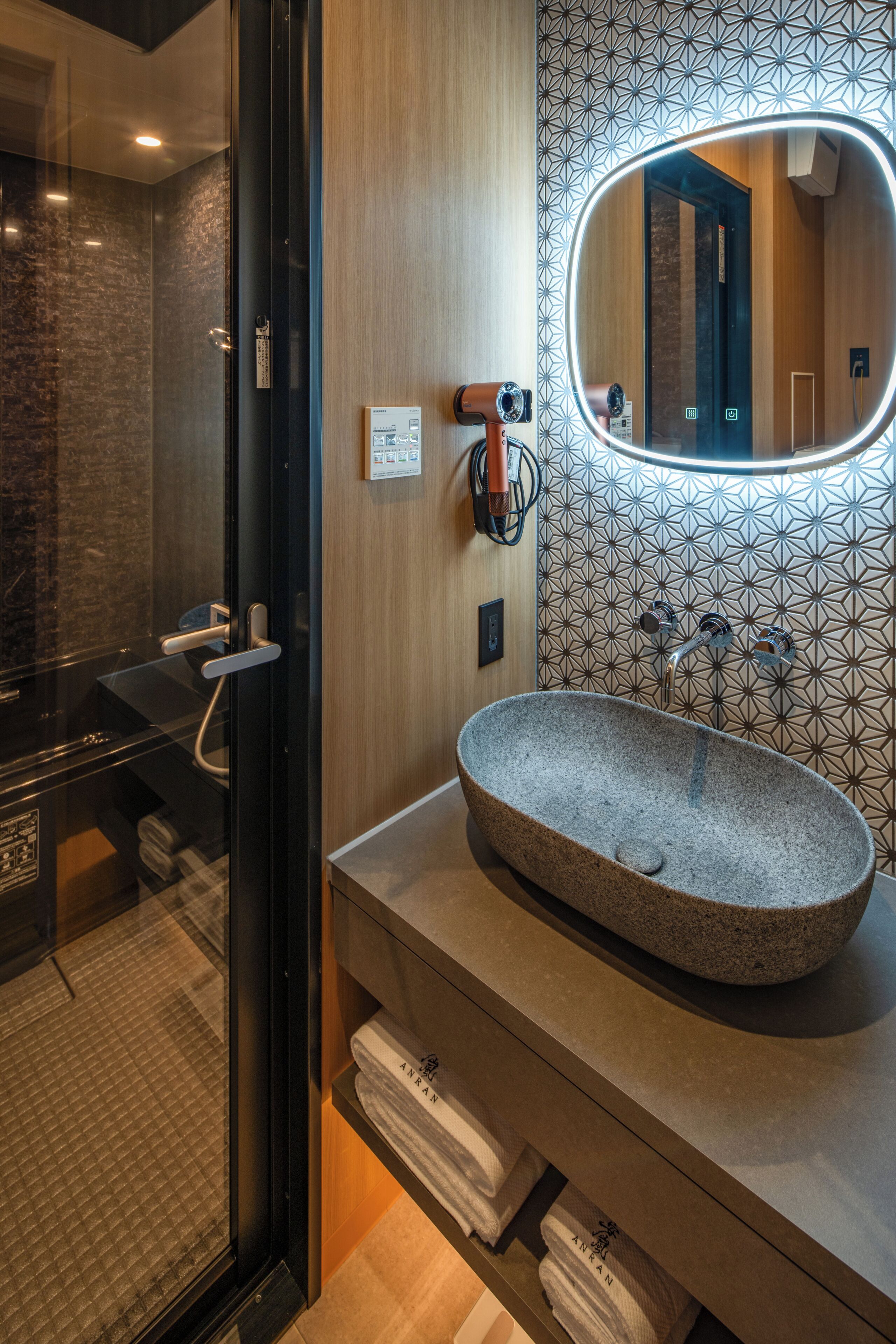 Un baño moderno con una bañera independiente, un espejo grande y un revestimiento de pared con diseño geométrico.