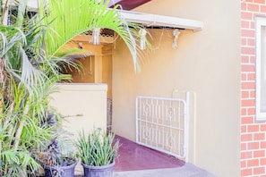 Una entrada protegida con un portón metálico, plantas en macetas y un muro con una ventana.