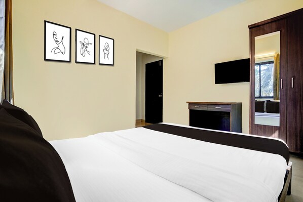 Habitación de hotel con una cama, un televisor de pantalla plana montado en la pared y tres obras de arte enmarcadas.