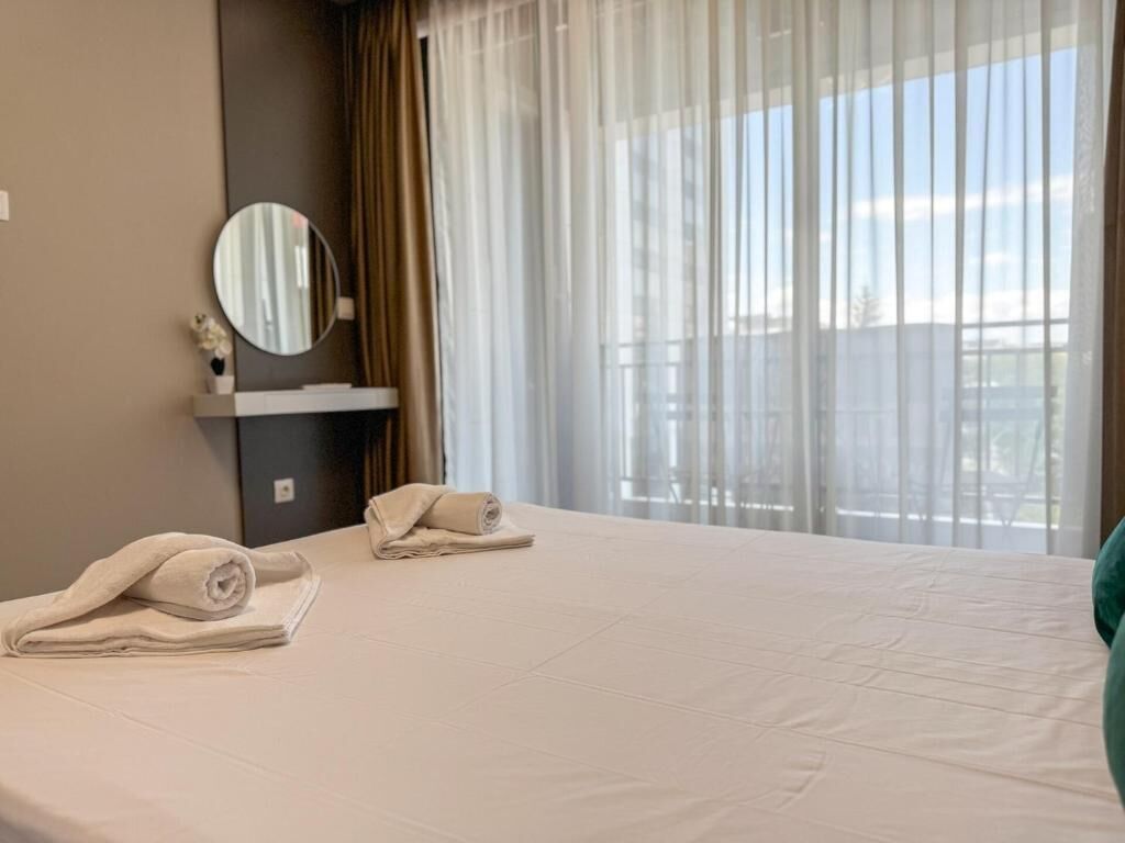 Hotellihuone, jossa on sänky, pyöreä peili ja ikkuna, jossa on läpikuultavat verhot.