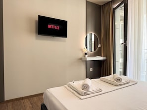 A hotel room with a bed, a TV mounted on the wall displaying 'NETFLIX', a round mirror, and a window with curtains. - Six StarS|Executive Business Suite|6 min to Centre (Пловдив)