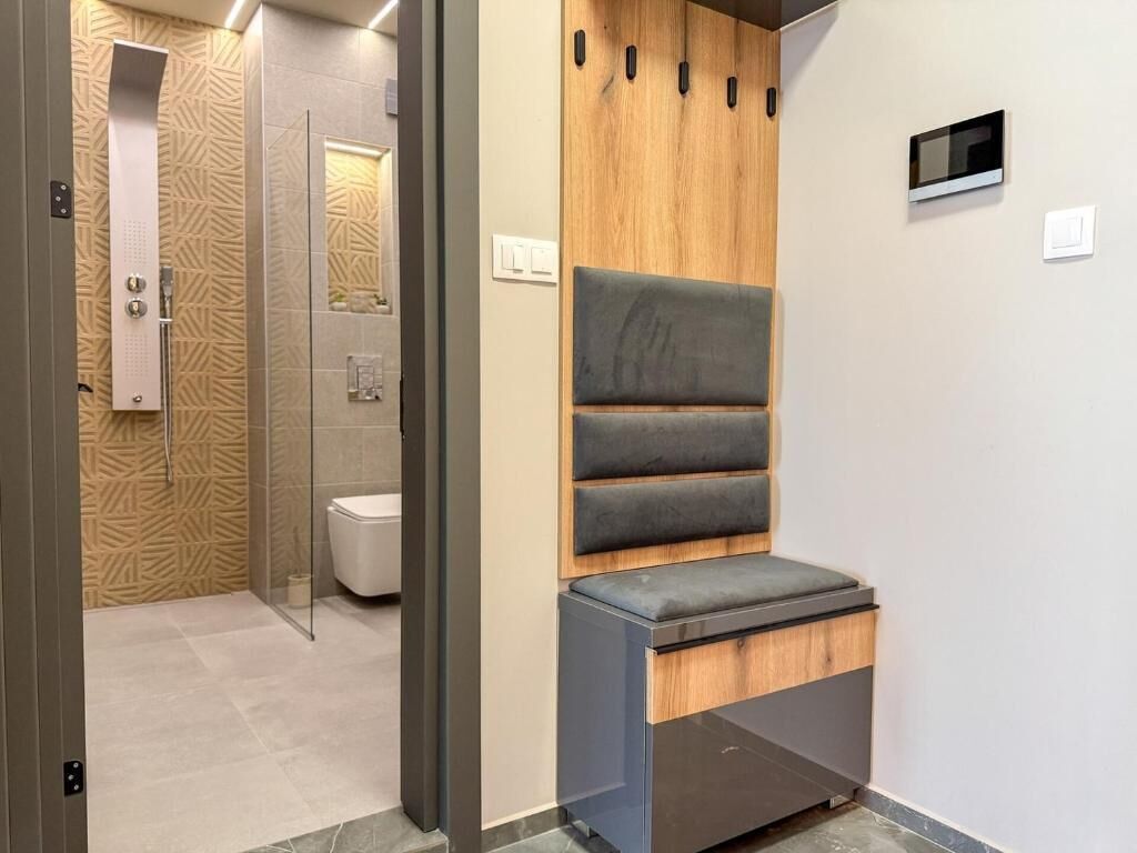 Een moderne badkamer met douche, toilet en een bankje met opbergladen.