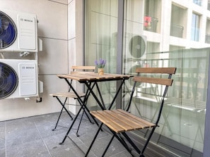 A balcony with two wooden chairs and a small table, a potted plant, and two Bosch air conditioning units.